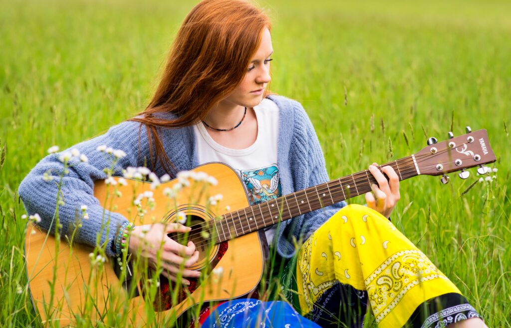 Elle Kay in a field of flowers playing guitar